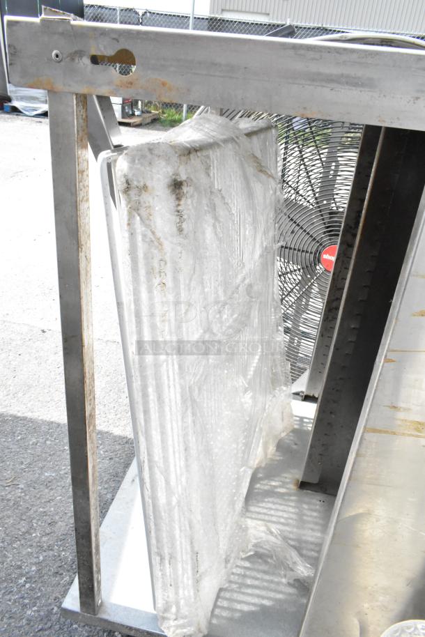 Stainless steel table with under shelf, rust marks visible, wrapped item and fan behind, used condition.