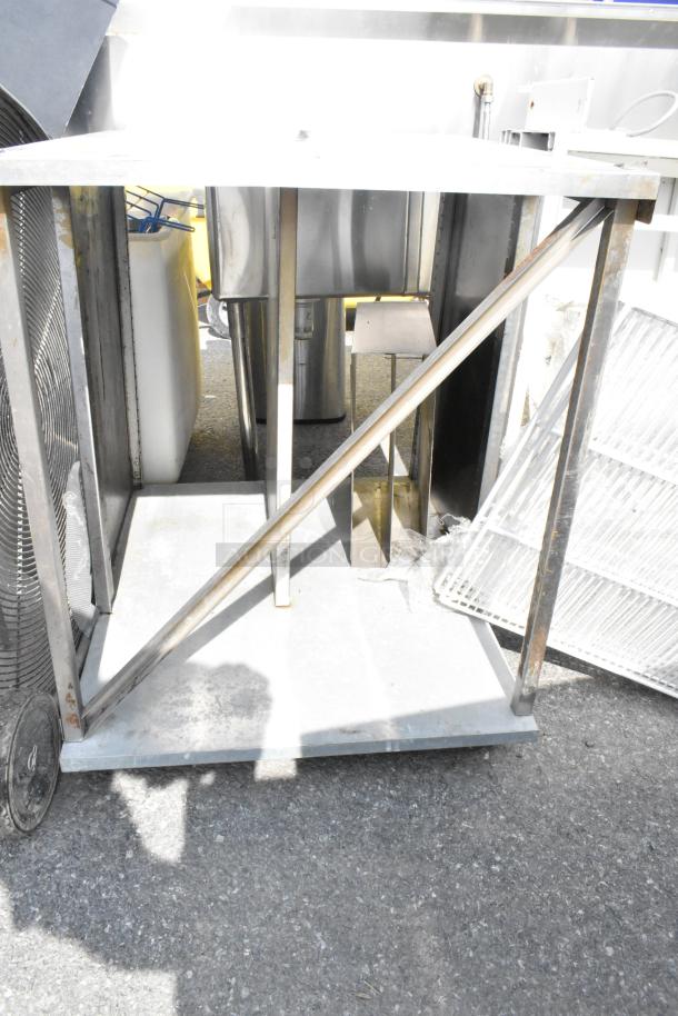 Industrial metal table with under shelf, showing wear. Side support bar visible. Ideal for storage or workspace use.