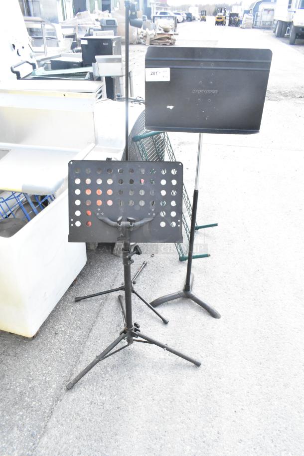 Three metal stands, including a Manhasset music stand, in used condition with adjustable features.