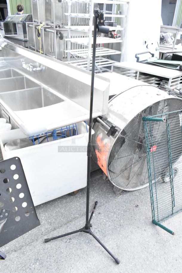 Adjustable black tripod stand, metal construction, used condition, suitable for music or equipment, placed outdoors.