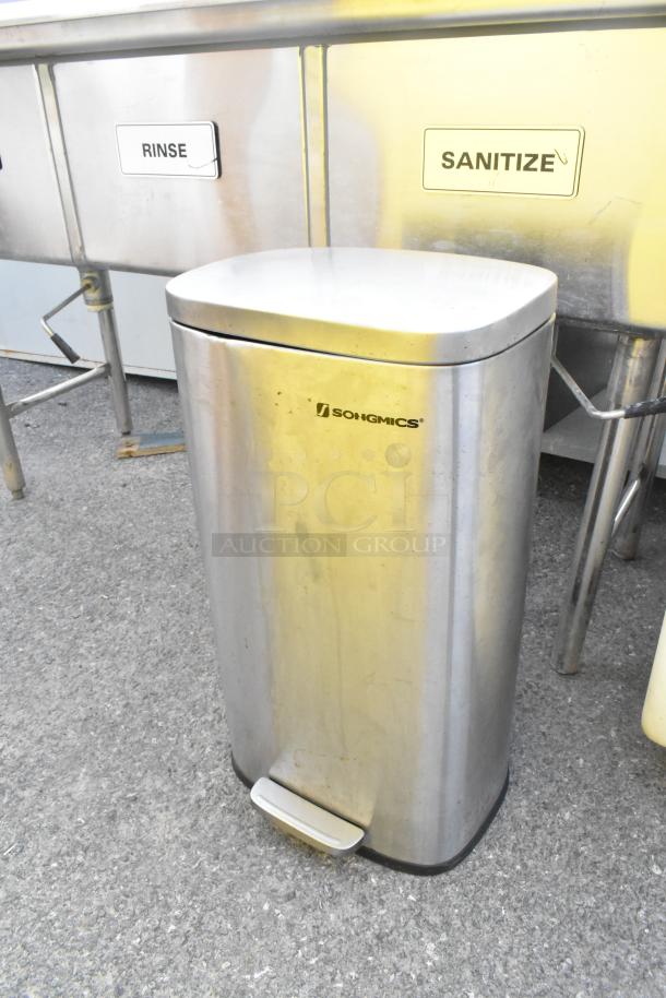 Stainless steel Songmics trash can with foot pedal, visible wear, near metal sinks labeled "Rinse" and "Sanitize."