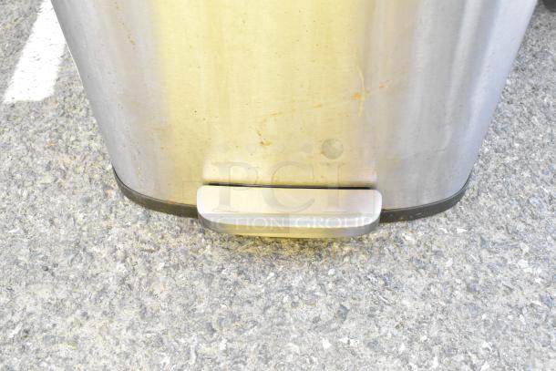 Songmics stainless steel trash can with pedal, visible wear, on outdoor concrete surface.
