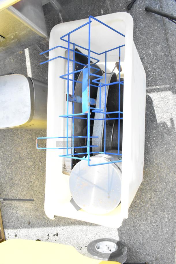 White poly trash can containing metal cookware and a blue wire rack, visible on concrete surface, fair condition.