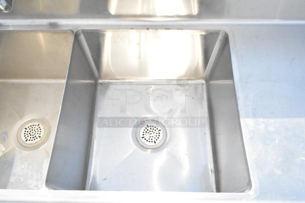 Commercial 3 bay sink with dual drain boards, stainless steel, visible wear, suitable for high-capacity kitchens.
