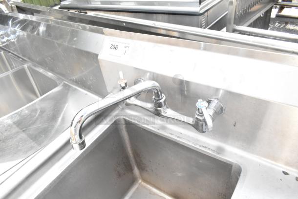 Commercial single bay sink with a right side drain board, stainless steel, dual faucet knobs, slight wear visible.