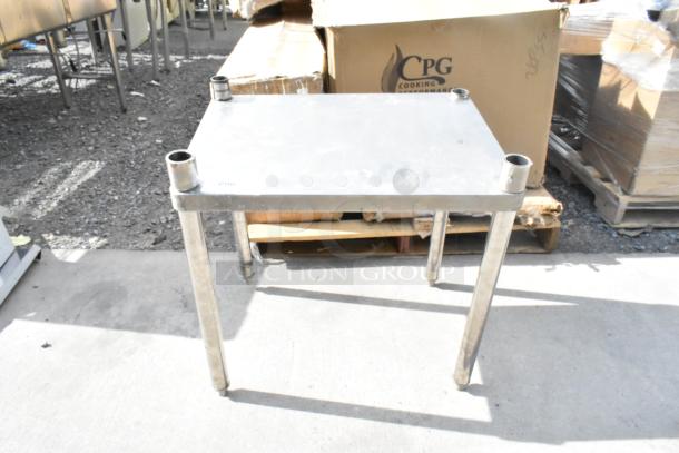 Stainless steel table with four cylindrical legs, lightly worn surface, ideal for industrial or kitchen use.