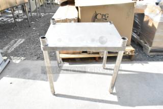 Stainless steel table with four cylindrical legs, lightly worn surface, ideal for industrial or kitchen use.