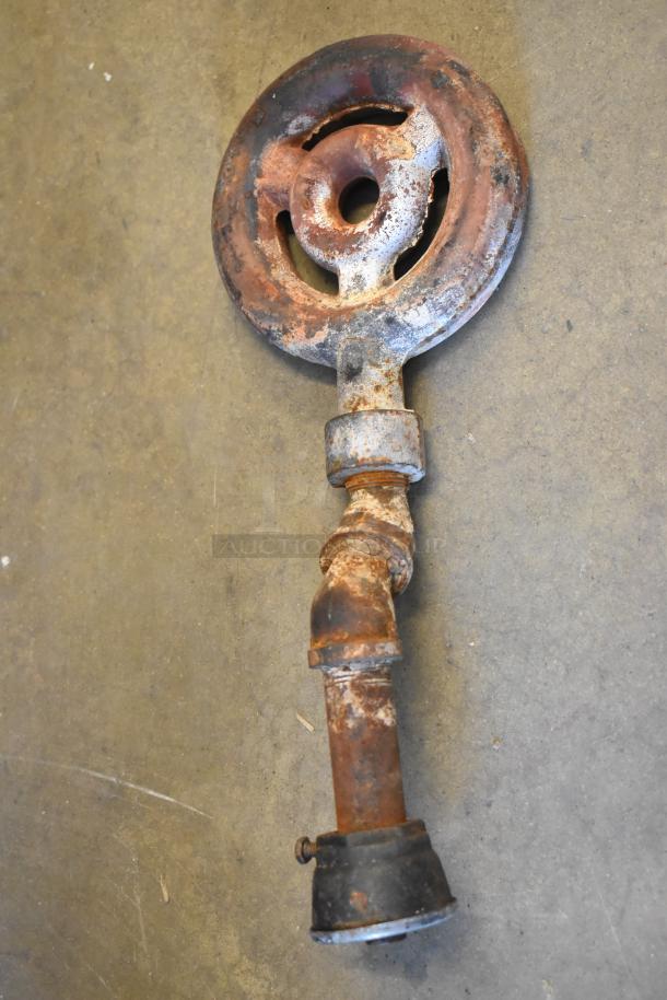 A rusty, vintage metal burner with attached pipe, showing wear and aging on a concrete floor.