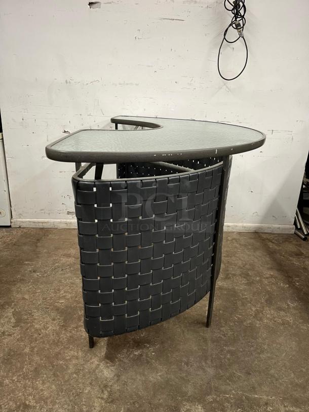 Curved outdoor bar with a woven textured design and glass top, showing slight signs of wear, suitable for patio use.