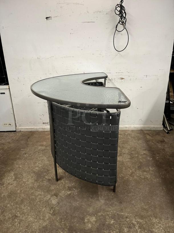 Curved outdoor bar with glass top, woven back design, metal frame, in good condition. Ideal for patios and gardens.