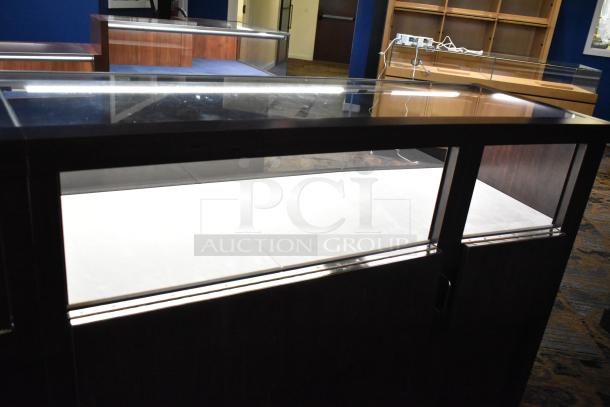 Wooden jewelry merchandising display case with glass top, dark wood finish, and interior lighting. Minor wear visible.