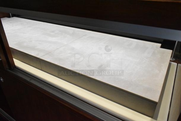 Wooden corner jewelry display case with two rear sliding doors, featuring a smooth, beige-slated countertop.