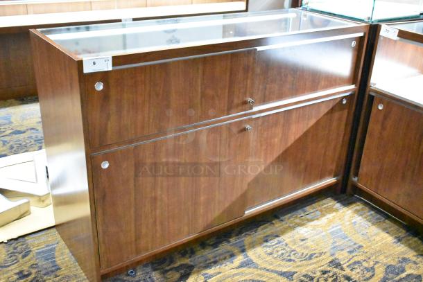 Wooden corner jewelry display case with glass top, two rear sliding doors, excellent condition, auction tag visible.