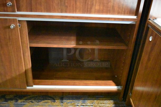 Wooden corner-style jewelry display case with two rear sliding doors, featuring a rich finish and two interior shelves; good condition.