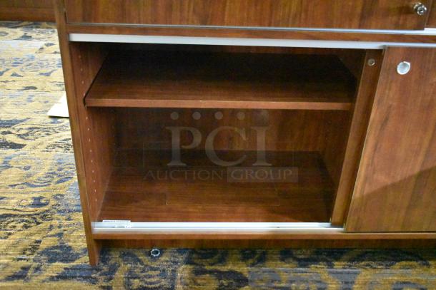 Wooden corner jewelry display case with two rear sliding doors, shelf space, and a polished finish. Suitable for showcasing items.