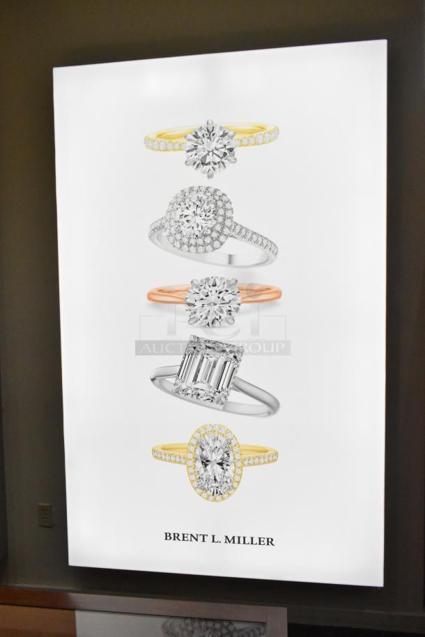 Wall-mounted SEG Systems LB-EDG-6D-W6-24 lighted picture display, showcasing diamond rings. Powers 110-277V. "Brent L. Miller" text.