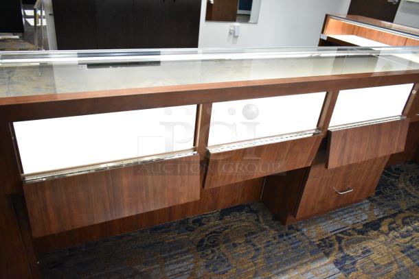 Lighted wooden jewelry display case with glass top, two drawers, and a polished finish. Ideal for showcasing items.