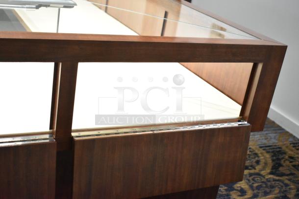 Lighted wooden jewelry merchandising display case with glass top, showing hinges and smooth wooden finish, in excellent condition.