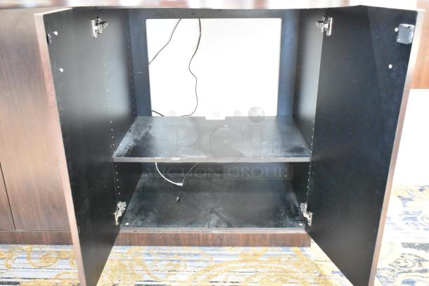 Wooden counter with four doors, open to reveal black interior shelving and cable access. Appears gently used.