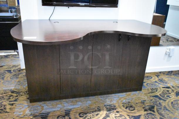 Dark wooden counter with four doors, sleek curved top, and two cutouts for cable management. Appears in good condition.