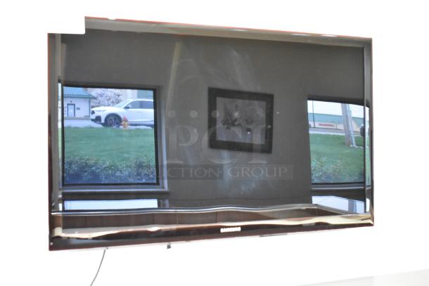 Samsung television, flat-screen, large size. Visible smudges on the screen. Wall-mounted, requiring removal tools.