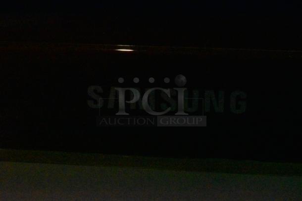 Samsung Television showing logo, condition not clearly visible in low light. Buyer must bring tools and manpower to remove.