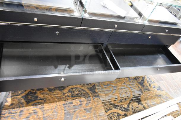 Black jewelry case with six rear drawers, glass top, and metal handles. Good condition. Buyer must remove; tools required.