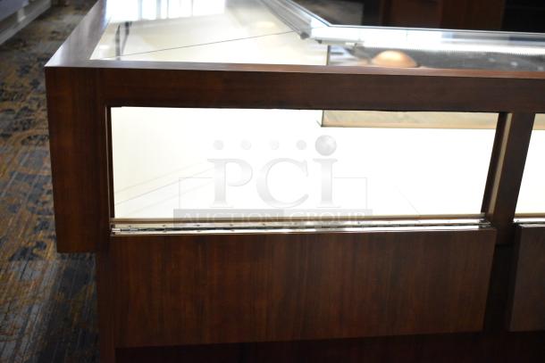 Wooden lighted jewelry case with glass top, featuring two rear doors. Buyers must bring tools for removal.