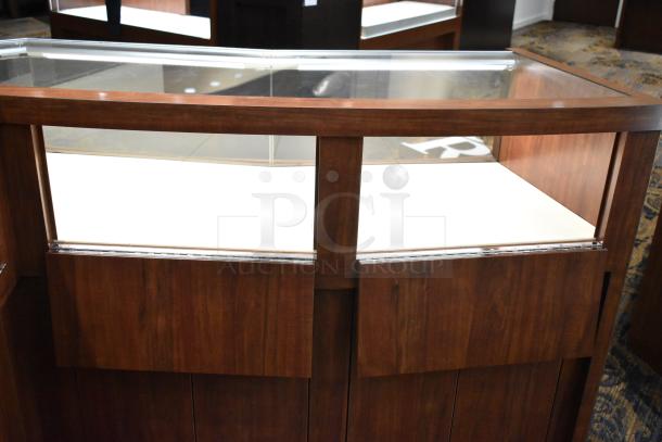 Wooden lighted jewelry case with glass top, featuring four rear doors. Excellent condition, buyer must remove.