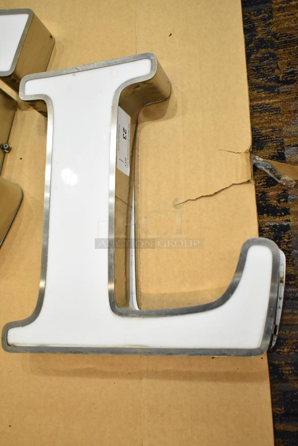White "L" letter with silver finish frame, shown on cardboard. Appears in good condition with a label indicating item number.