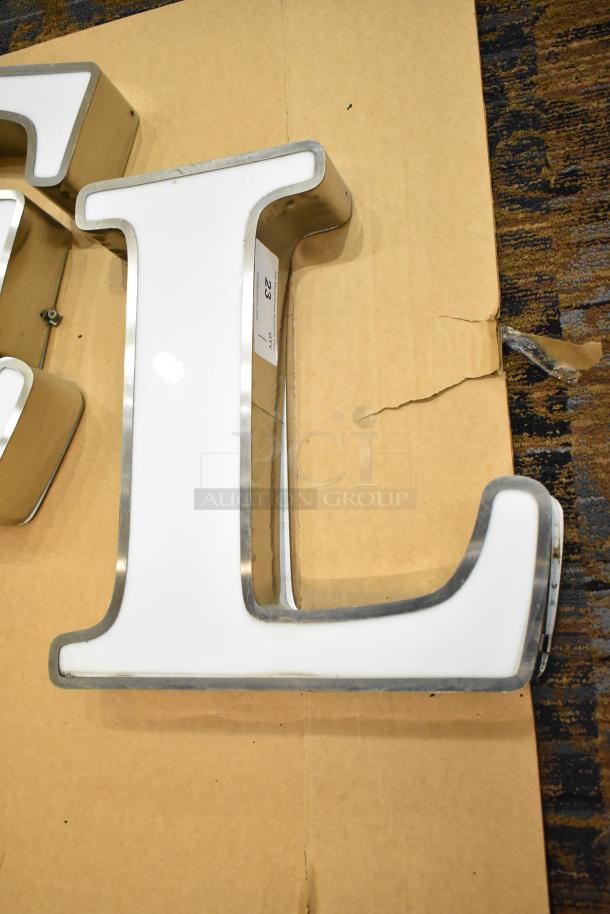 White "L" letter with silver finish frame, in good condition, on cardboard. Marking visible: "23" on label inside.