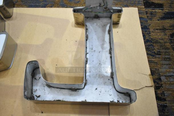 White letter "L" with silver finish frame, showing wear and some dirt, resting on a cardboard surface.