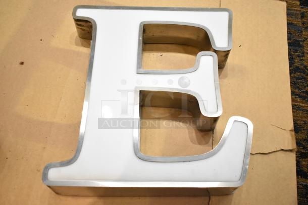 White letter "E" with a silver finish frame, mounted on cardboard. Good condition, used for signage or decor.