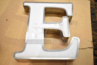 White letter "E" with a silver finish frame, mounted on cardboard. Good condition, used for signage or decor.