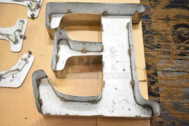 White letter "E" with silver finish frame, pre-owned. Visible wiring indicates previous use for signage. Condition shows wear and minor dirt.
