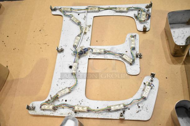 White letter "E" with silver finish frame featuring LED wiring, showing signs of wear; ideal for signage use.
