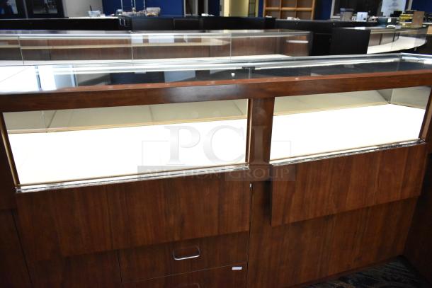 Lighted wooden jewelry display case with glass top, two rear sliding doors, and storage. Buyer must remove.