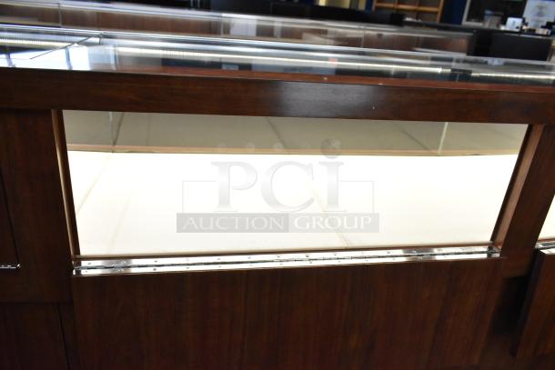 Lighted wooden jewelry display case with glass top, two rear sliding doors. Buyer must bring tools for removal.