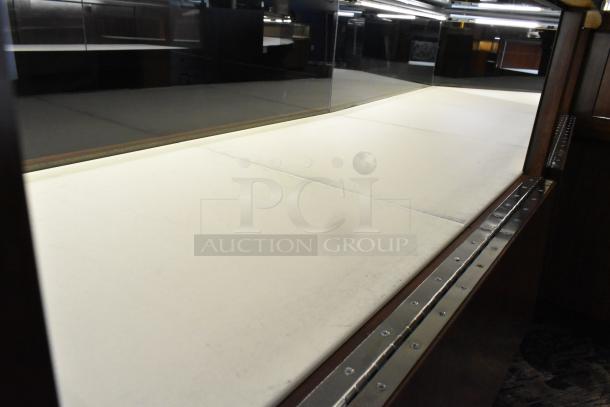 Lighted wooden jewelry display case with two rear sliding doors, needs removal. Brown wood, white interior. Good condition.