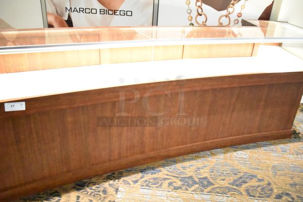 Lighted wooden jewelry display case with 6 rear doors, 3 drawers, glass top, and natural finish, Marco Bicego branding.