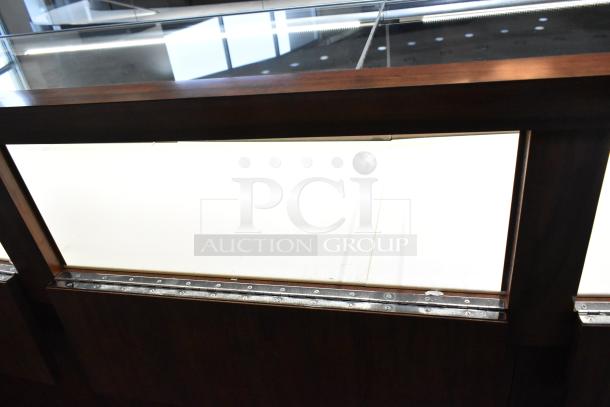 Lighted wooden jewelry display case with glass top, six rear doors, and three drawers. Buyer must bring tools for removal.