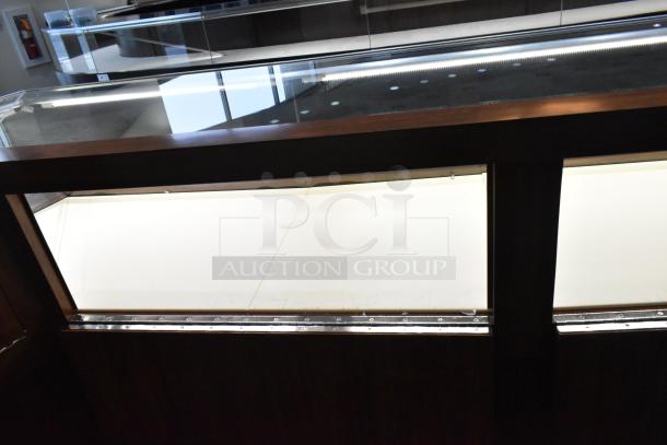 Lighted wooden jewelry display case with glass top, 6 rear doors, and 3 drawers. Needs tools and manpower for removal.