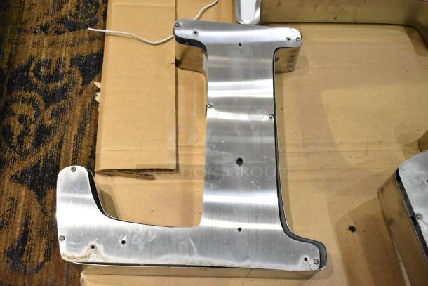 White "L" letter with silver finish frame, featuring visible screws and wiring, on a cardboard surface.