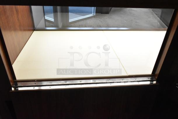 Lighted wooden jewelry display case with two rear doors, in good condition. Buyer must bring tools for removal.