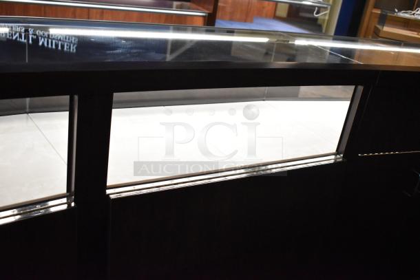 Lighted curved wooden jewelry display case, with rear doors and drawers, glass top. Buyer removal required.