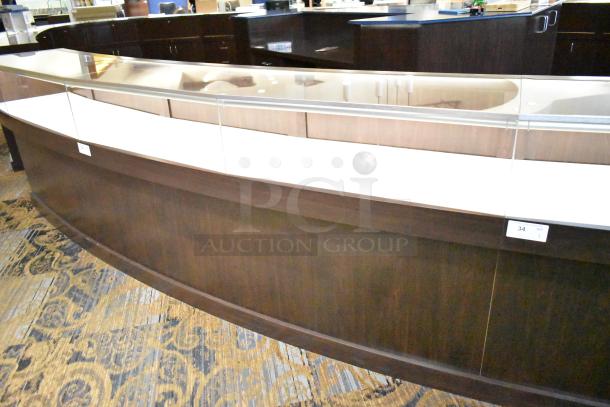Curved wooden jewelry display case with lighting, rear doors, and drawers. Buyers must bring tools for removal.