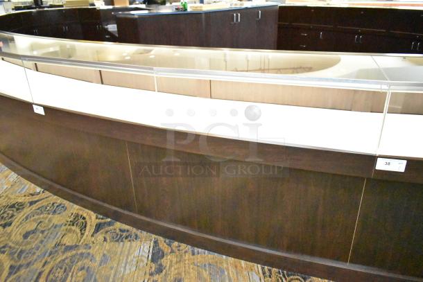 Lighted curved wooden jewelry display case with glass top, four rear doors, dark wood finish. Buyer must remove.