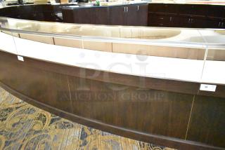 Lighted curved wooden jewelry display case with glass top, four rear doors, dark wood finish. Buyer must remove.