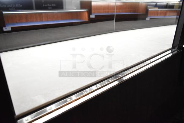 Lighted curved wooden jewelry display case with glass front, four rear doors, and interior shelving. Buyer must remove.