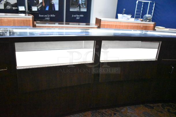 Lighted curved wooden jewelry display case with glass top, four rear doors, and removable condition; buyer to remove.